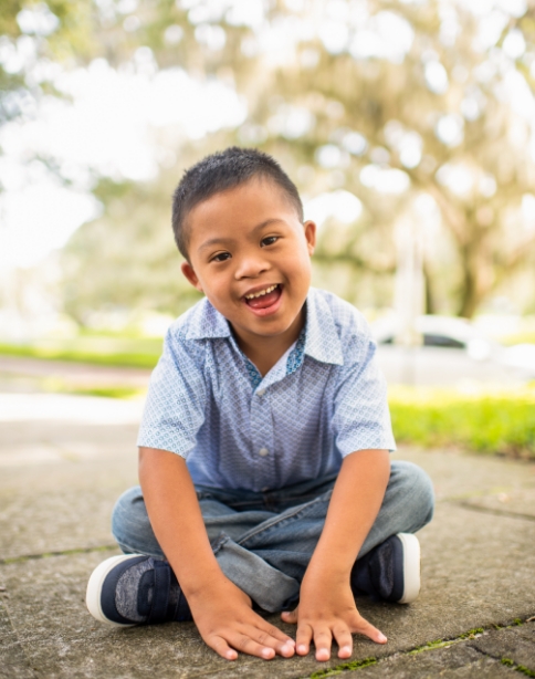child in dress shirt smiling sitting on sidewalk